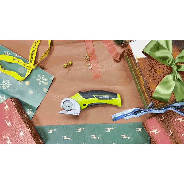 A Cordless Electric Cutter with a self-sharpening stainless steel blade is displayed on wrapping paper amidst holiday gift boxes, ribbon, scissors, gold bells, and a gift tag. The scene evokes an easy and festive holiday gift-wrapping or crafting experience made simple with this lightweight tool.