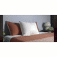 A neatly made bed features brown and white pillows, including the Adjustable Height Pillow for added comfort, topped with a brown quilted blanket. Beside the bed, a side table holds a white lamp and small plants against a gray wall.