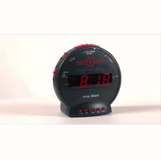 The Alarm Bomb Extra Loud Alarm Clock With Bed Shaker, in black with red buttons and digital display showing 8:18, is ideal for heavy sleepers and stands on a white surface.
