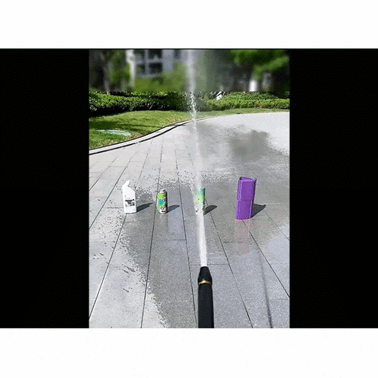 A stream from the Powerful Speed Washer Hose Nozzle knocks over four upright boxes and cans lined up on wet outdoor pavement, with grass and trees in the background.
