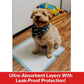 A small, tan dog wearing a plaid bandana sits on a Drawstring Pee Pad (Includes 25 Pads) indoors. Behind the dog is a wooden crate with pet supplies. Text below reads: Ultra-Absorbent Layers With Leak-Proof Protection! Featuring advanced odor control technology for a fresher home.