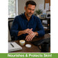 A man in a blue shirt applies Hempvana Cocoa Butter pain relief cream to his hand while sitting at an office desk with a computer, notebook, and coffee mug. The text at the bottom reads: Nourishes & Protects Skin!.