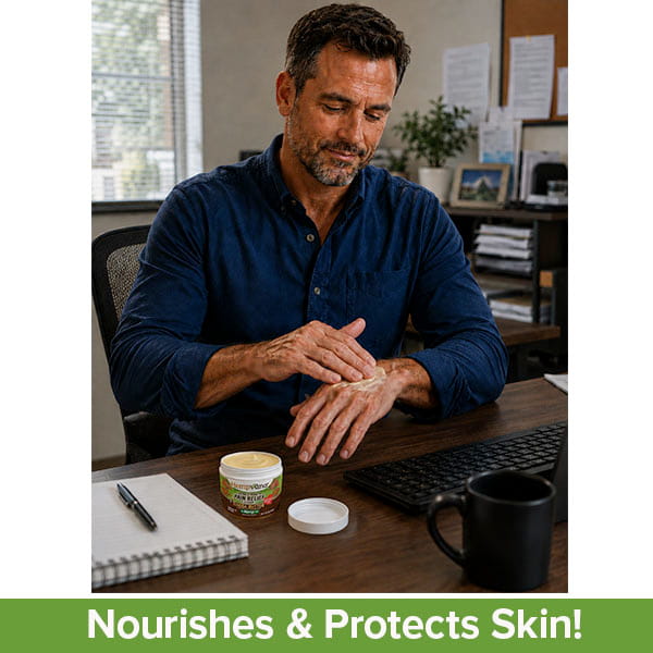 A man in a blue shirt applies Hempvana Cocoa Butter pain relief cream to his hand while sitting at an office desk with a computer, notebook, and coffee mug. The text at the bottom reads: Nourishes & Protects Skin!.