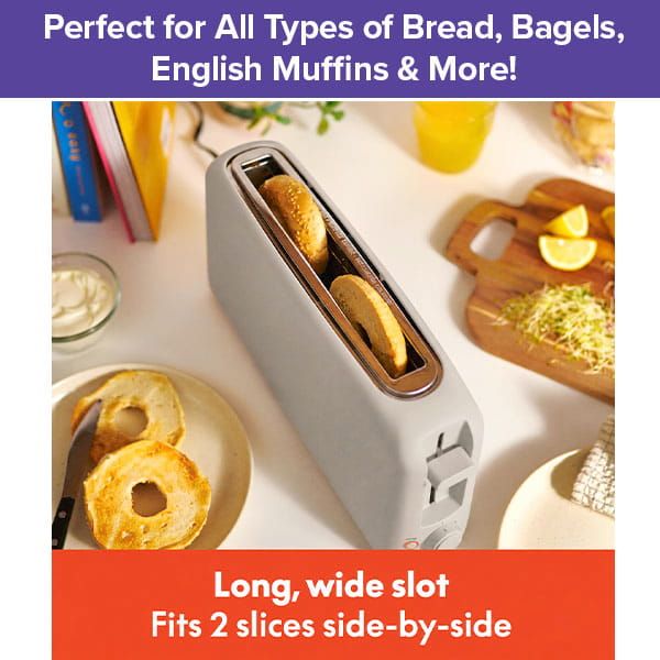 A Slim Toaster Fits Anywhere sits on a kitchen counter, holding two bagel halves in its long, extra-wide slots. Sliced bagels, a cutting board, butter, and toppings are arranged around the toaster. Text above reads: Perfect for All Types of Bread, Bagels, English Muffins & More!.