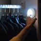 Close up of woman's hand touching an Atomic Beam TapLight attached to the wall in a closet, the light is on.