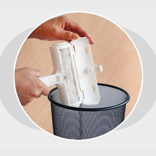 Close up of woman's hands holding a Pet Hair Remover over a trashcan with the pet hair compartment open and dumping the hair out