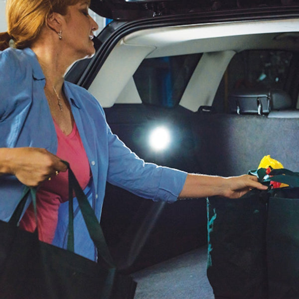 Woman getting grocery bags from trunk and an Atomic Beam Taplight is lit up on the interior of the trunk
