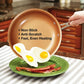 Close up of woman's hand turning a Red Copper Pan to the side and some sunny side up eggs are sliding onto a green plate with bacon on it
